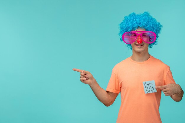 Día de los inocentes chico sonriendo despojado rosa gafas de sol nariz roja pelo azul payaso manos divertidas señalando