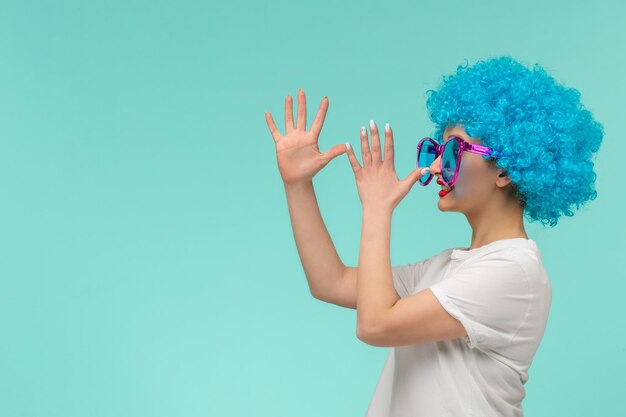 Día de los inocentes payaso niña sonriente tocando la punta de la nariz grandes gafas de sol azules traje divertido cabello azul