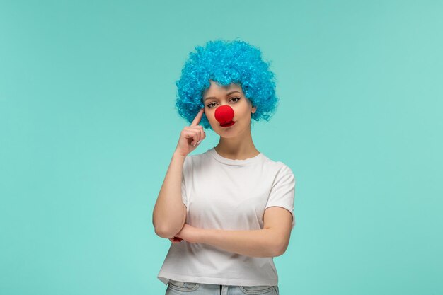 Día de los inocentes pensando gesto chica dedo a cabeza con nariz roja en un traje de payaso cabello azul