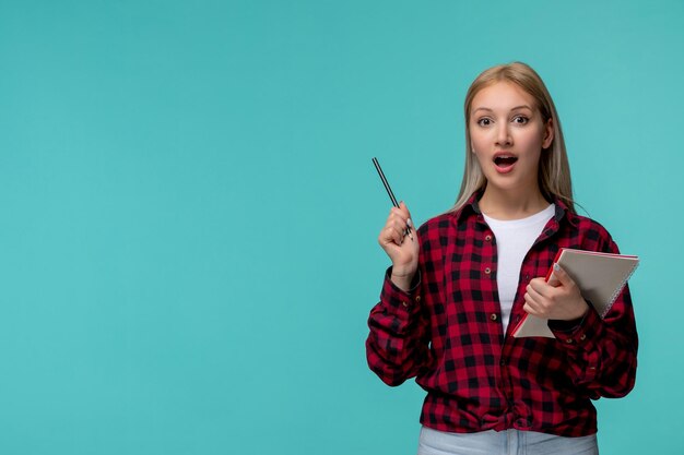 Día internacional de los estudiantes joven linda chica en camisa roja a cuadros emocionada con lápiz y cuaderno