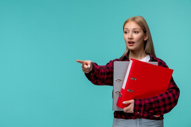 Día internacional de los estudiantes linda chica rubia con camisa roja a cuadros apuntando al frente con carpetas de archivos