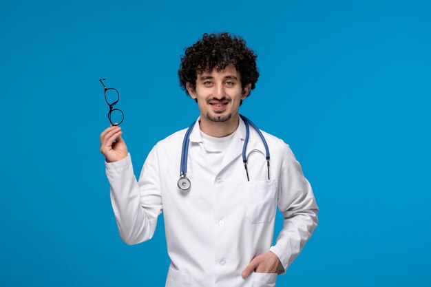 Día de los médicos chico lindo morena rizada en bata de laboratorio quitándose las gafas y sonriendo