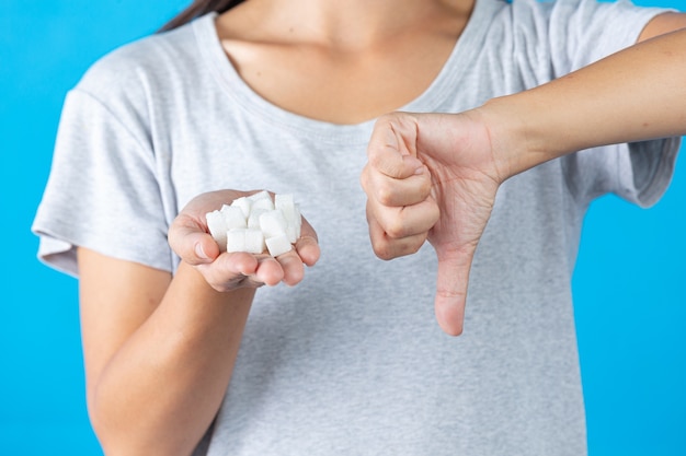 Foto gratuita día mundial de la diabetes; mano sosteniendo cubos de azúcar y pulgar hacia abajo en otra mano