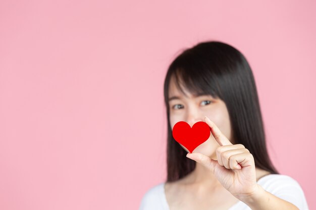 Día mundial de la diabetes; mujer sosteniendo corazón rojo en la pared rosa