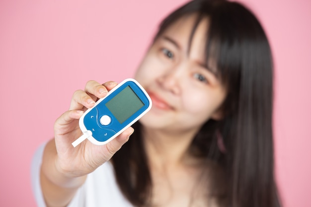 Día mundial de la diabetes; Mujer sosteniendo medidor de glucosa en pared rosa