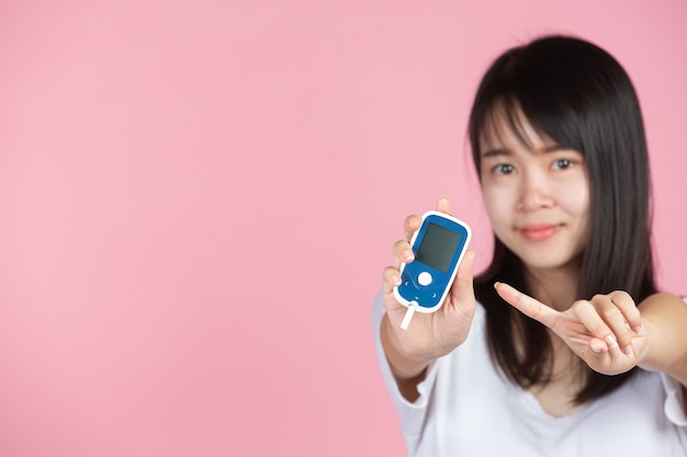 Día mundial de la diabetes; Mujer sosteniendo medidor de glucosa en pared rosa