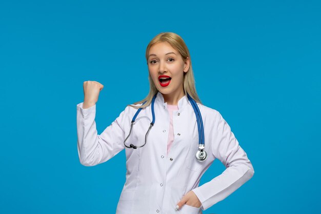 Día mundial del médico emocionado rubio lindo joven médico con el estetoscopio en la bata de laboratorio