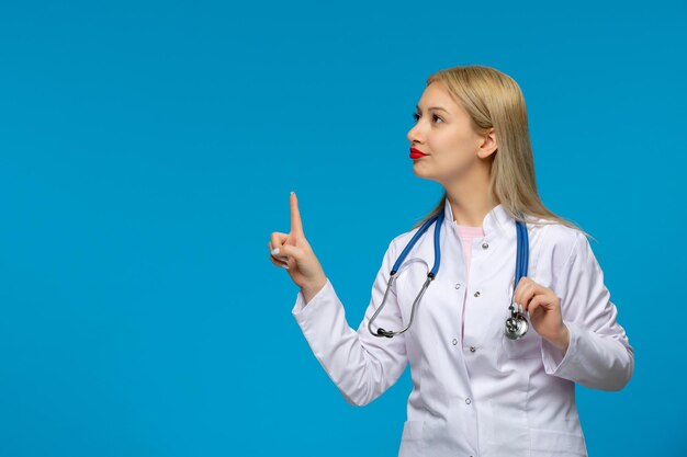Día mundial del médico linda doctora rubia que muestra la señal de stop con el estetoscopio en la bata de laboratorio