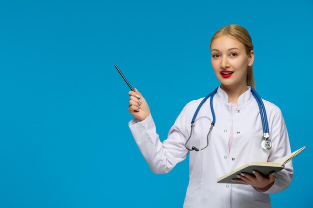 Día mundial del médico médico sonriente sosteniendo un bolígrafo y un libro con el estetoscopio en la bata de laboratorio