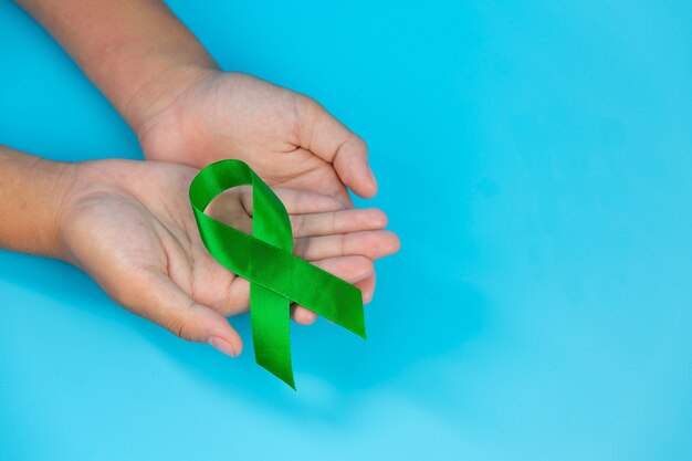Día mundial de la salud mental. Cinta verde puesta en manos del ser humano sobre fondo azul.