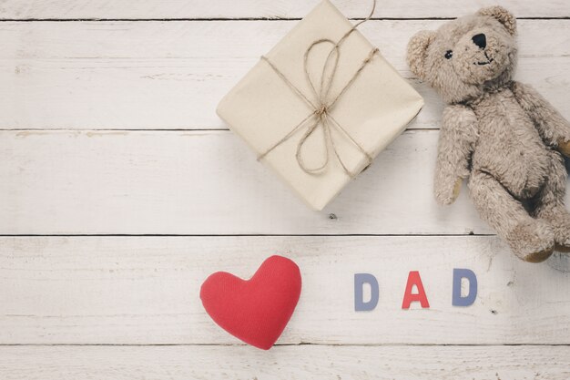 Día de padre feliz de la vista superior. Corazón rojo con la palabra &quot;PAPÁ&quot; en el fondo de madera. Presente y muñeca del oso para los regalos.