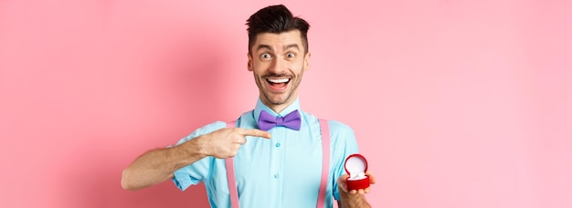 Foto gratuita día de san valentín alegre joven va a hacer propuesta apuntando con el dedo al anillo de compromiso y smil