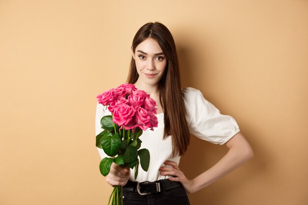 Día de San Valentín hermosa novia sosteniendo rosas rosadas y mirando a cámara mujer joven recibe flo ...