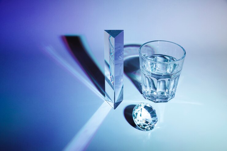 Foto gratuito diamante espumoso; prisma; vaso de agua con sombra sobre fondo azul oscuro
