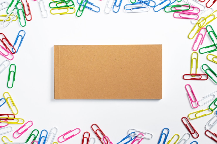Foto gratuito diario de cuaderno en blanco con tapa dura de cartón en el centro y pernos de papel de colores alrededor aislado en blanco.