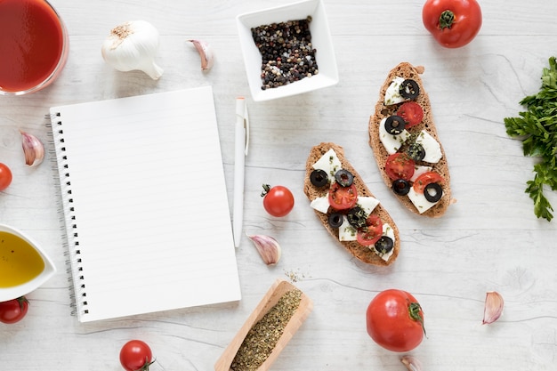 Diario espiral en blanco y bruschetta con ingrediente en mesa de madera