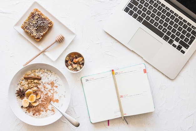 Foto gratuita diario con lápiz; ordenador portátil; y desayuno saludable en el telón de fondo