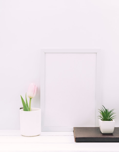 Diario; planta; Flor de tulipán con marco de fotos en blanco en mesa blanca
