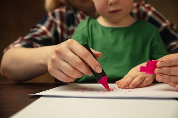 Dibujo con rotuladores de colores. Primer plano de las manos de mujeres y niños haciendo cosas diferentes juntos. Familia, hogar, educación, infancia, concepto de caridad. Madre e hijo o hija, estudiando.