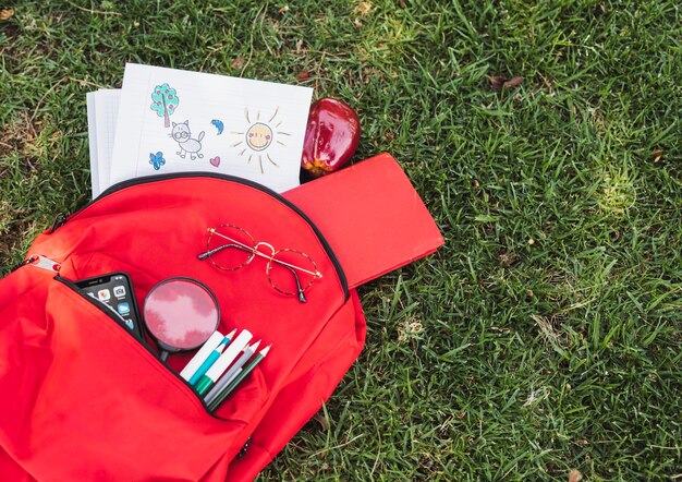 Dibujos cerca de mochila roja con papelería y teléfono inteligente.