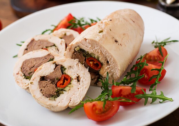 Dieta al horno rollos de pollo rellenos de hígado, chile y hierbas con una ensalada de tomates y rúcula. Menú dietético Nutrición apropiada.