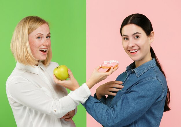 Dieta. Concepto de dieta. Alimentos saludables y útiles. Hermosas mujeres jóvenes eligiendo entre frutas y pastel poco saludable en el estudio. Emociones humanas y conceptos de comparación