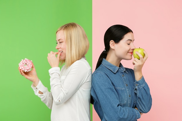 Dieta. Concepto de dieta. Alimentos saludables y útiles. Hermosas mujeres jóvenes eligiendo entre frutas y pastel poco saludable en el estudio. Emociones humanas y conceptos de comparación