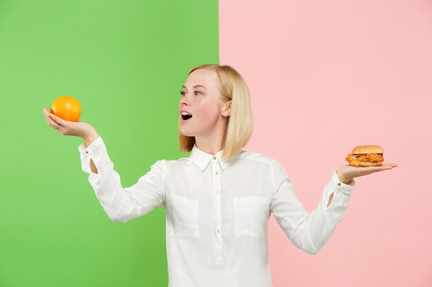 Dieta. Concepto de dieta. Comida sana. Hermosa joven eligiendo entre frutas y comida rápida poco saludable