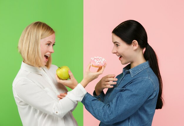 Dieta. Concepto de dieta. Comida sana. Hermosas mujeres jóvenes eligiendo entre frutas y pastel poco saludable