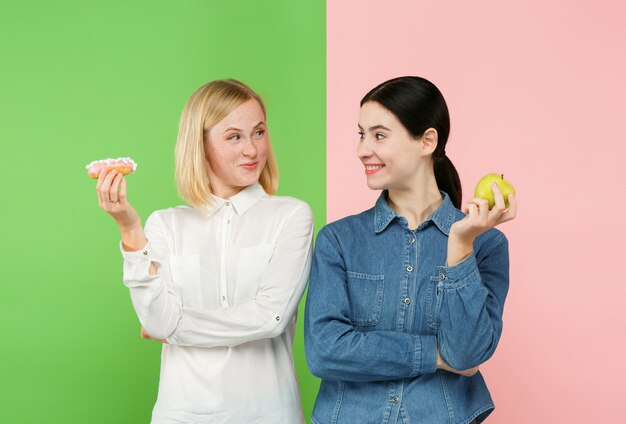 Dieta. Concepto de dieta. Comida sana. Hermosas mujeres jóvenes eligiendo entre frutas y pastel poco saludable