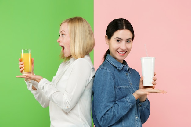 Dieta. Concepto de dieta. Comida sana. Hermosas mujeres jóvenes eligiendo entre jugo de naranja y bebida dulce carbonatada poco saludable