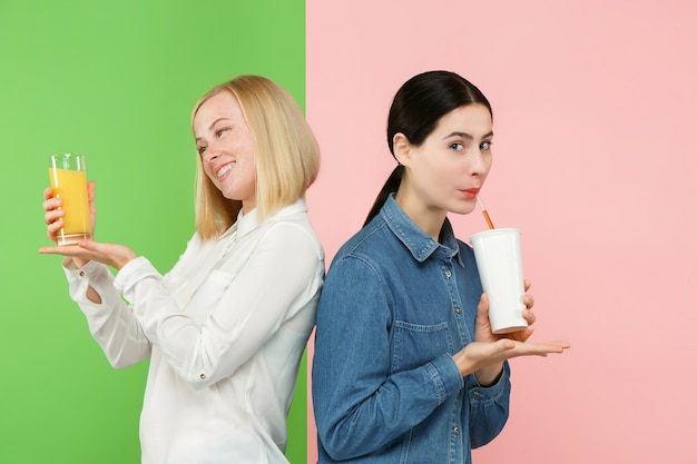 Dieta. concepto de dieta. comida sana. hermosas mujeres jóvenes eligiendo entre jugo de naranja y bebida dulce carbonatada poco saludable