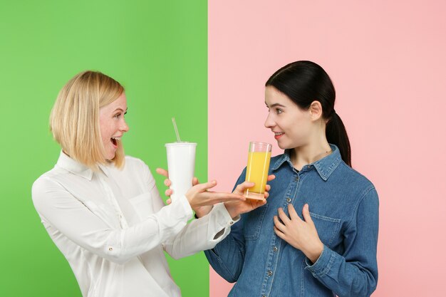 Dieta. Concepto de dieta. Comida sana. Hermosas mujeres jóvenes eligiendo entre jugo de naranja y bebida dulce carbonatada poco saludable