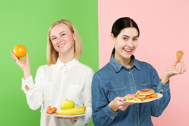 Dieta. Concepto de dieta. Comida sana. Hermosas mujeres jóvenes que eligen entre frutas y comida rápida poco saludable