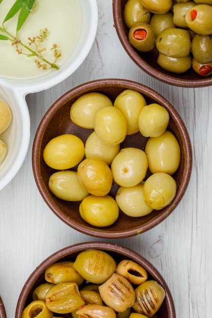 Foto gratuita diferentes aceitunas con hojas y aceite de oliva en una arcilla y cuencos blancos sobre madera blanca, primer plano.