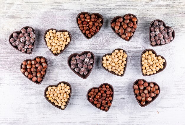 Diferentes avellanas en una vista superior de cuencos en forma de corazón sobre una mesa de madera blanca