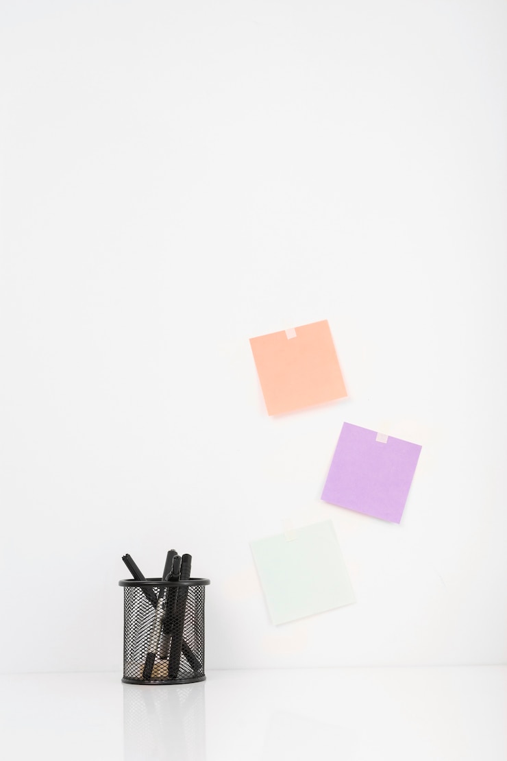 Foto gratuito diferentes bolígrafos en el soporte cerca de coloridas notas adhesivas pegadas en la pared