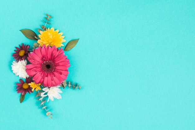 Diferentes flores con hojas en mesa azul