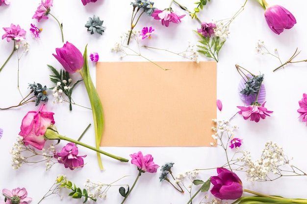 Diferentes flores con papel en blanco sobre mesa.