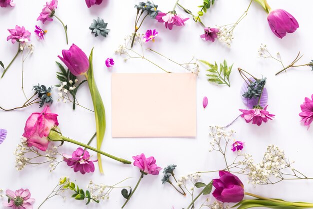 Diferentes flores con papel sobre mesa blanca.