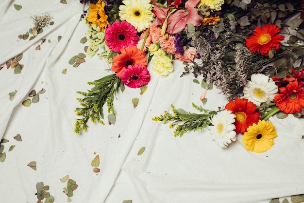 Diferentes tipos de coloridas flores de gerbera y hojas sobre tela blanca