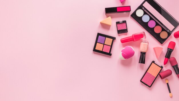 Diferentes tipos de cosméticos esparcidos sobre mesa rosa.