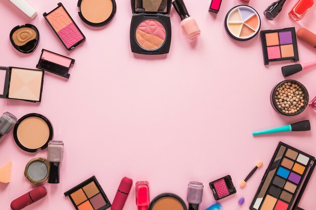 Diferentes tipos de cosméticos esparcidos sobre mesa rosa.
