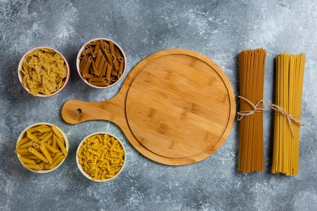 Diferentes tipos de espaguetis crudos con tablero de madera.