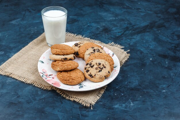 Diferentes tipos de galletas, leche en un mantel sobre un fondo azul oscuro. vista de ángulo alto.