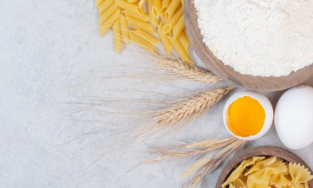 Diferentes tipos de pasta cruda con harina y huevo crudo sobre superficie de mármol.