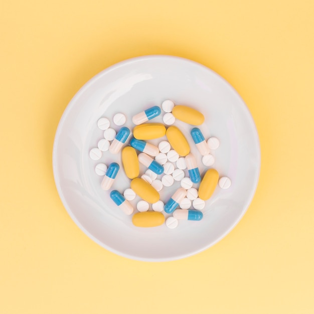 Diferentes tipos de pastillas en un plato blanco sobre fondo amarillo