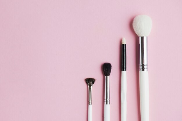 Diferentes tipos de pinceles de maquillaje en una fila sobre fondo rosa