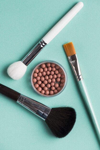 Diferentes tipos de pinceles de maquillaje con perlas bronceadas sobre fondo verde