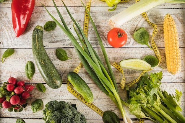 Foto gratuita diferentes tipos de verduras frescas con cinta métrica en el escritorio de madera